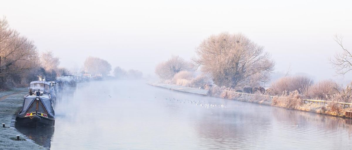 A narrowboat moored on a still canal on a frosty, misty winter morning